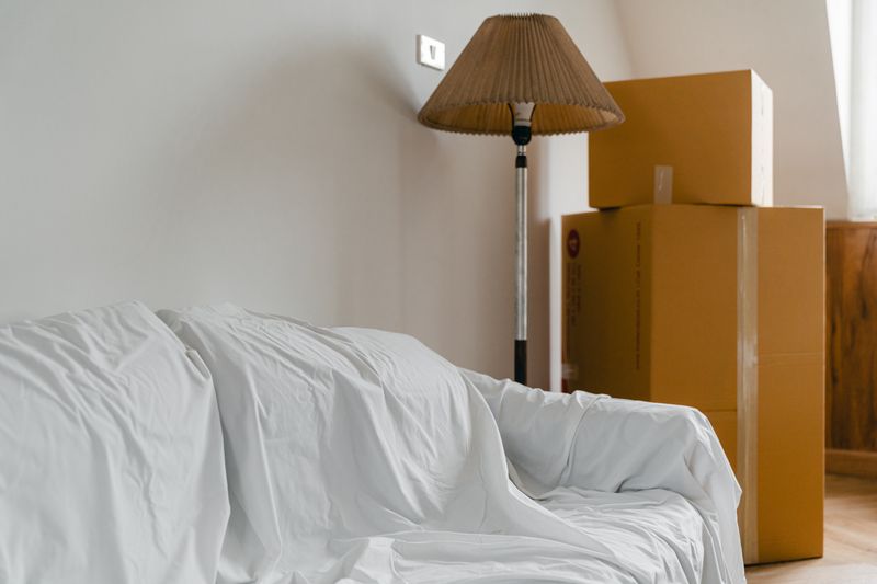 Covered furniture and packed boxes in a bright new home living room